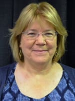 Kristie Ketchum an older white woman smiling at the camera wearing glasses and a multicolored blue scoop neck shirt.