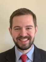 Erik Nordlof, a smiling Caucasian male in his mid-thirties with short, neatly trimmed brown hair and a trimmed beard. He is dressed in a dark suit, a light blue dress shirt, and a red tie.