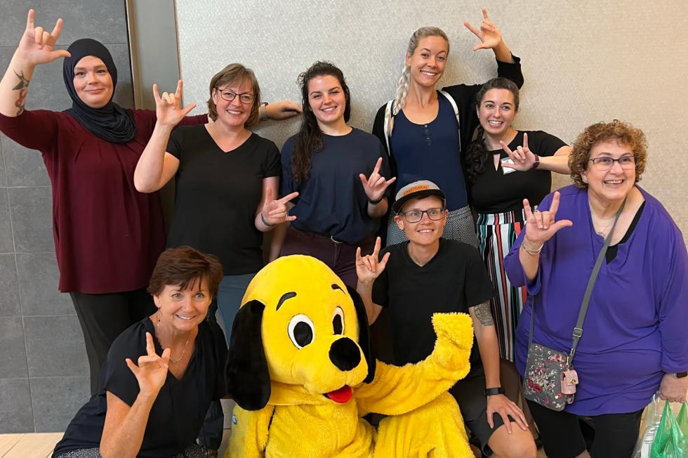 The NVRC team making the I love you sign with their mascot, a person in the costume of a large yellow dog