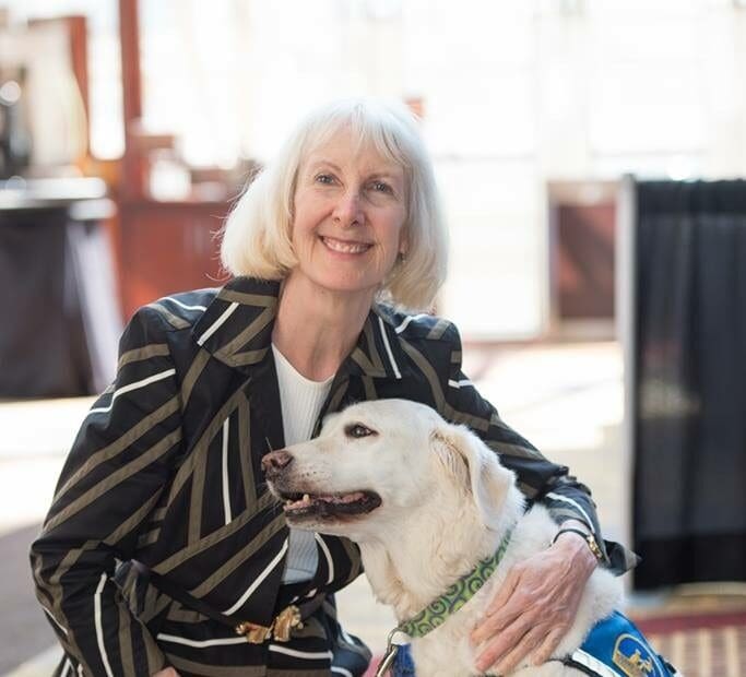 Cheryl kneeling with her arm around a white dog