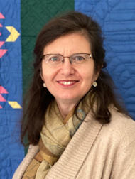 Barbara in a tan cardigan and scarf against a blue background