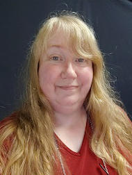 Debbie in a red shirt with a half-smile and a dark background