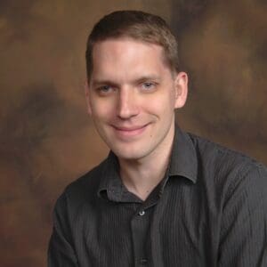 photo of Jason corning, male presenting with short dark hair, wearing a brown collared shirt.